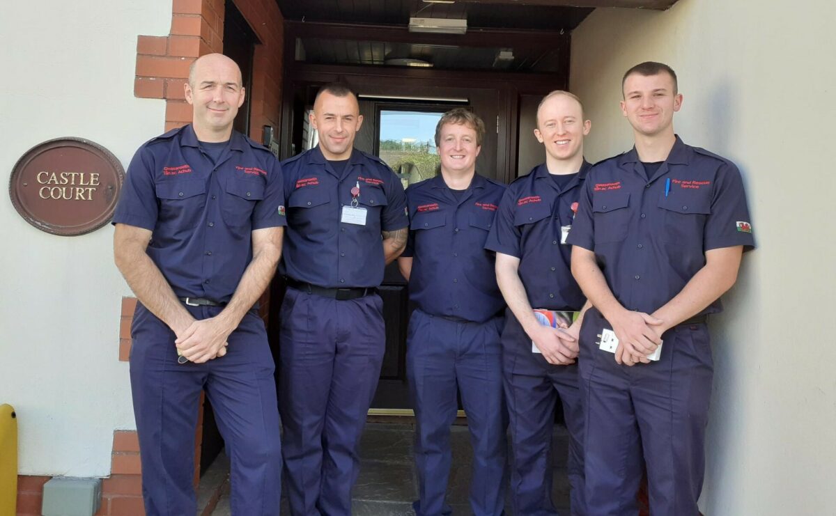 A group of firemen standing outside a block of apartments